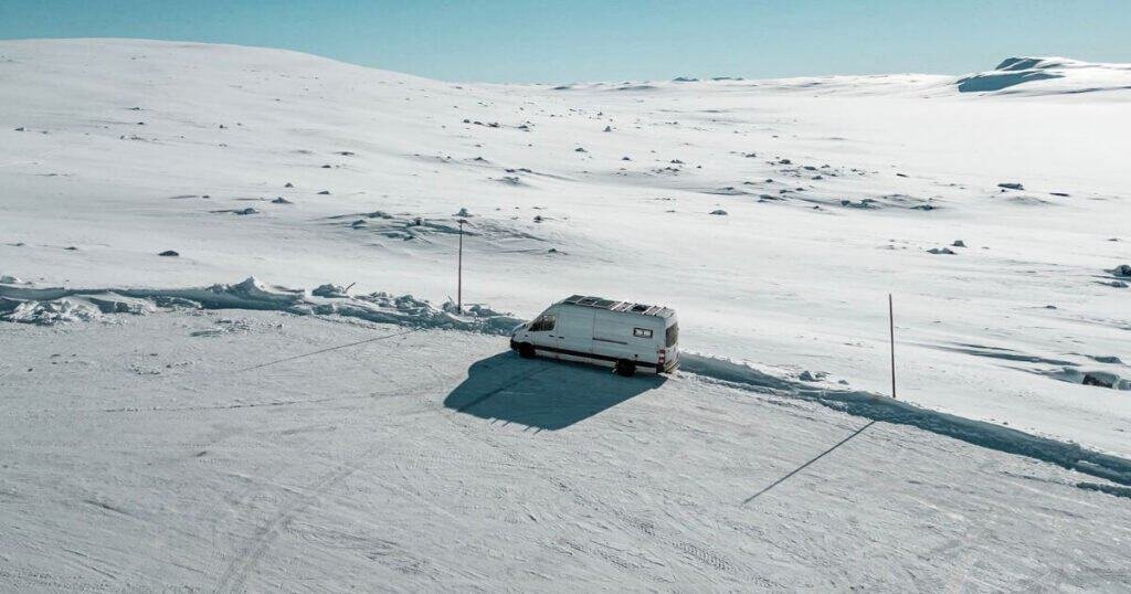 White campervan amongst a flat snowy landscape in Norway. Living in a van during winter in Norway takes you to these vast snow covered moonscapes.