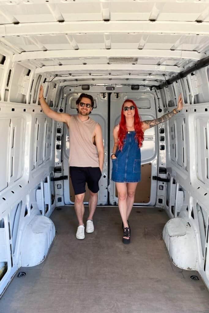 Man and woman stood in an empty Mercedes Sprinter panel van, pre vanlife conversion.