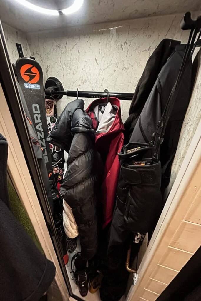 Looking into a shower cubicle with lots of wet ski gear hung up and ski leaning against the walls. This is used as a heating room to dry this gear during winter vanlife. 