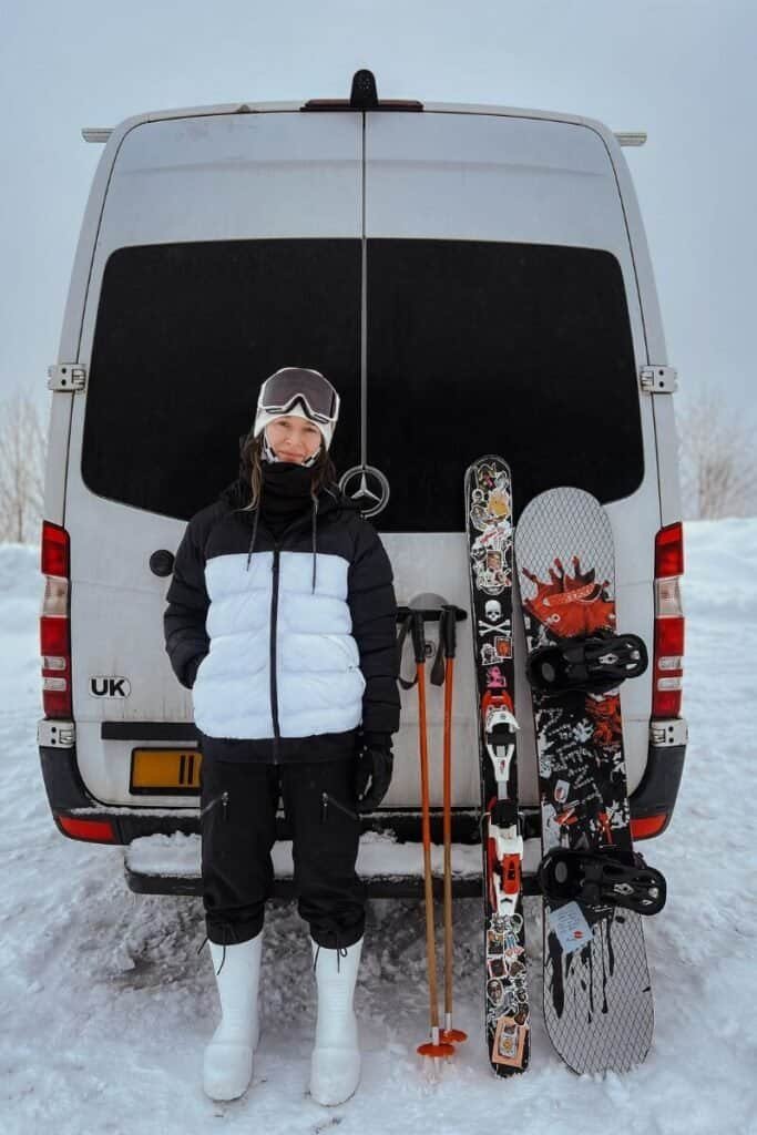 Woman standing at the back of her converted campervan with a set of skis and a snowboard in Voss, Norway. 