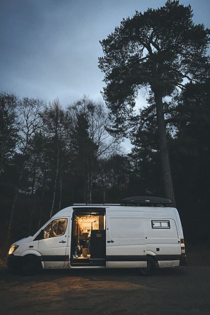 Campervan parked with the sliding door open and a golden glow from inside, at nighttime in Scotland.