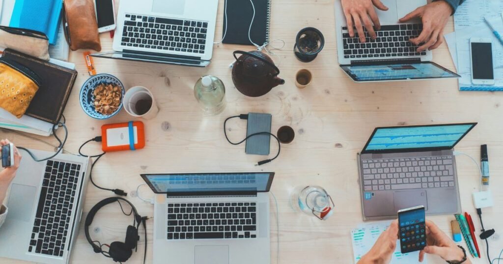 Lots of laptops, phones and coffee mugs in a co-working space.