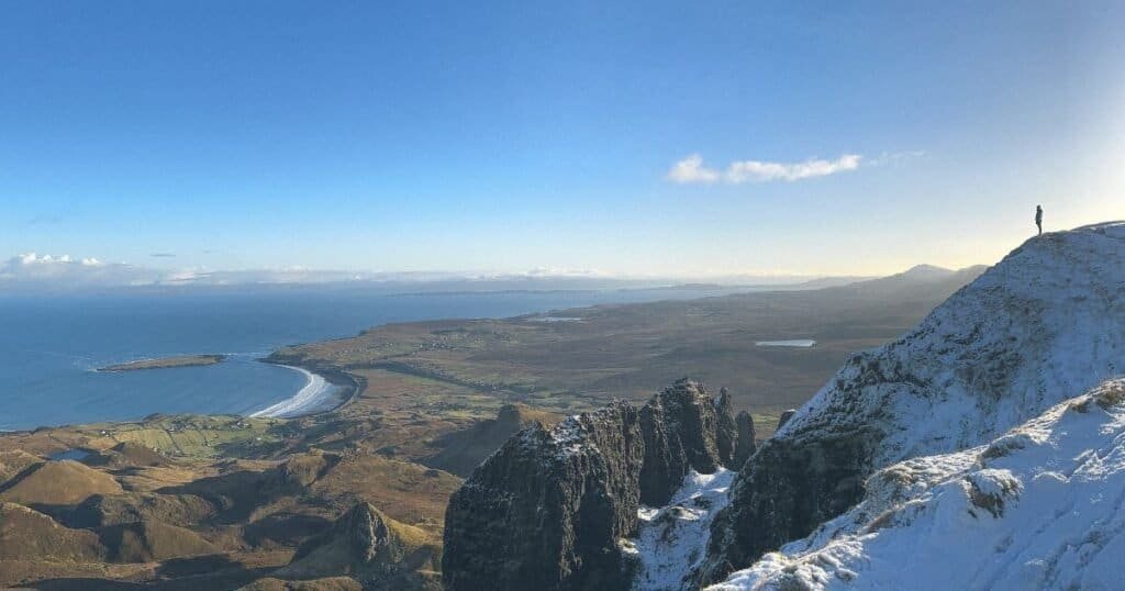 A small figure on top of a snow covered hill, staring out towards the ocean in the Isle of Skye, Scotland in winter. 