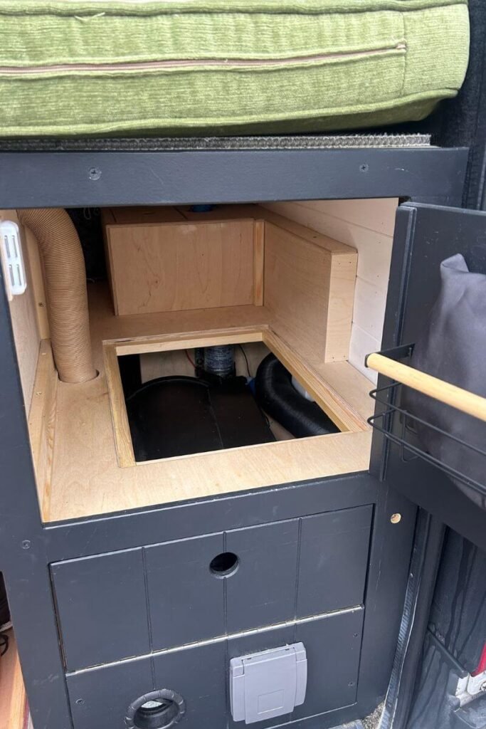 Looking inside a wooden hatch in the back of a campervan revealing a black heater with brown ducting pipework coming out out of it. This is a great option heating option to distribute heat around a van during winter vanlife