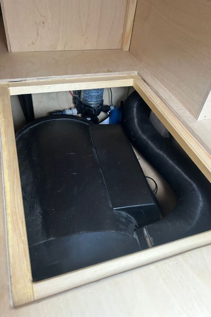 A black boiler encased in the wooden framework of a campervans interior, perfect for keeping a van warm during winter vanlife