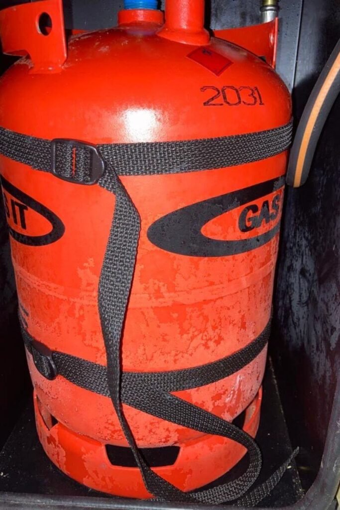 A close up of a red LPG gas tank inside a black box covered in frost  