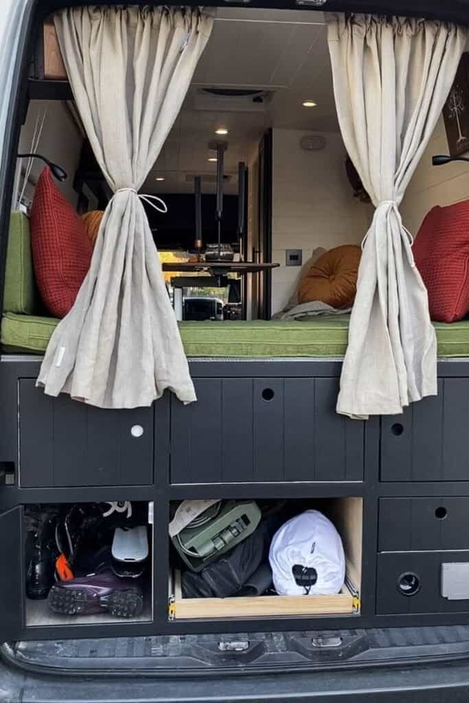 Large garage space at the back of a converted sprinter van. Cosy decor in black, green and orange hues. 