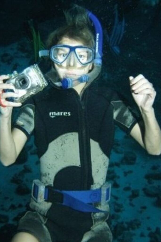 Woman underwater in scuba gear holding a camera.