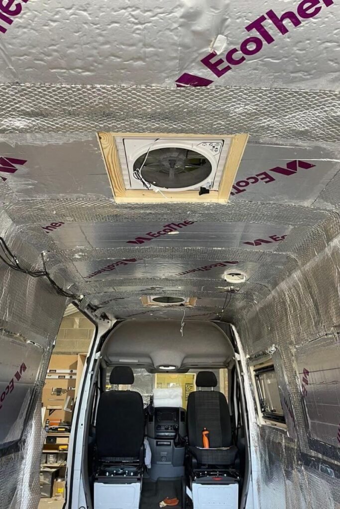 This inside of a panel van being converted for winter vanlife. There are vent fans in the roof and silver insulation foil can be seen covering the walls