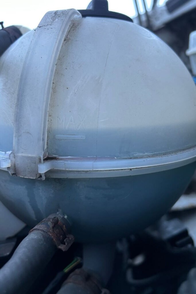 A close up under the hood of a van of the side of the engine coolant chamber. A blue liquid can be seen inside filling it up to the 'MAX' line. 