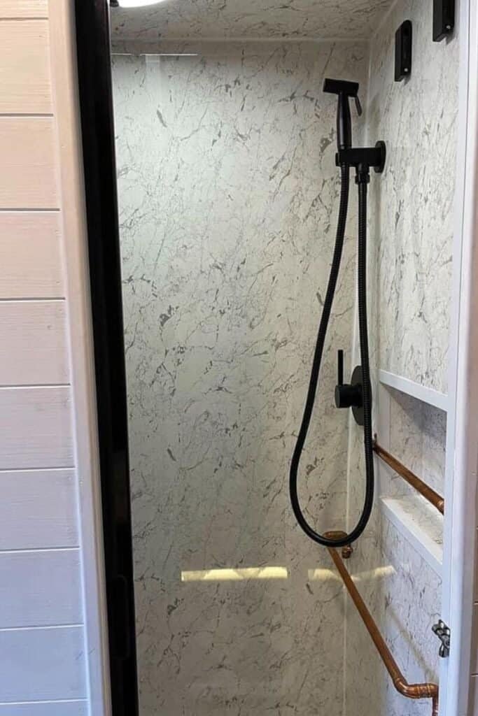 Looking into a white shower cubicle with white marble walls, a copper railing and a black shower head