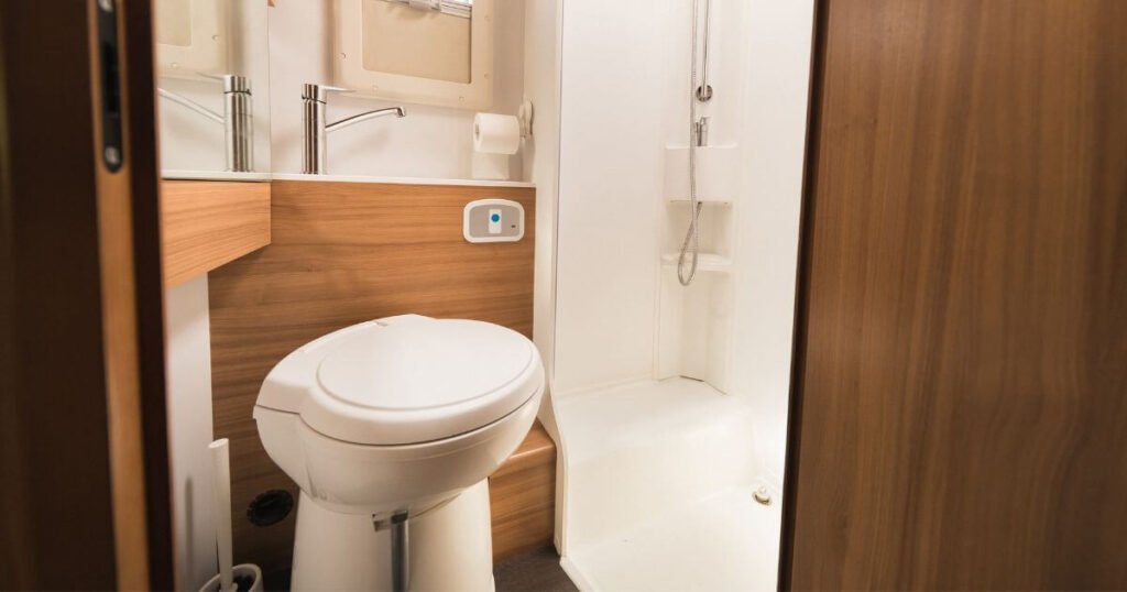 A White Plumbed in Camper Van Toilet in a vans shower cubicle. It looks very similar to a regular house toilet. 