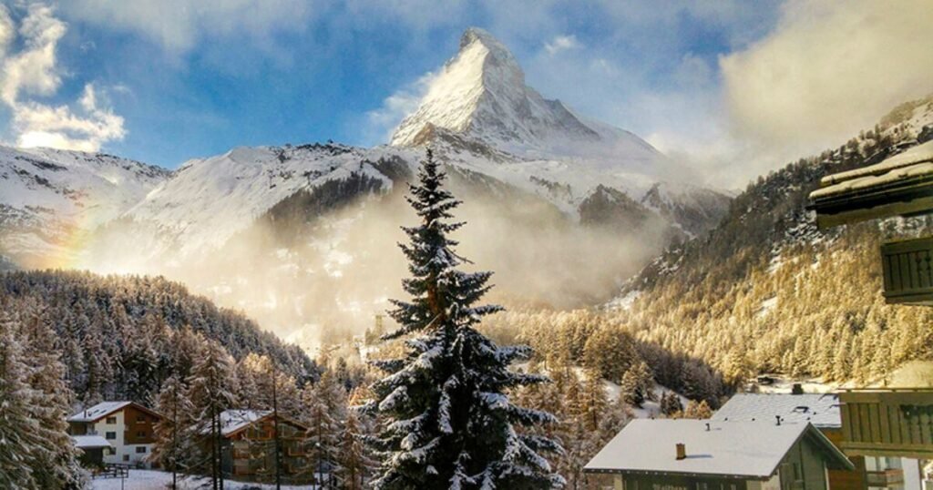 A snow covered Matterhorn behind a haze and rainbow in Zermatt in December.